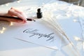 Female master of lettering of ink writes word on paper, sitting Royalty Free Stock Photo