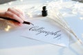 Female master of lettering of ink writes word on paper, sitting Royalty Free Stock Photo
