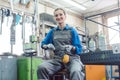 Female mechanic sitting in metal workshop looking into camera