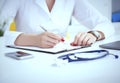 Female medicine doctor hand holding silver pen writing something on clipboard and working laptop closeup. Physician Royalty Free Stock Photo