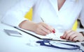 Female medicine doctor hand holding silver pen writing something on clipboard and working laptop closeup. Physician Royalty Free Stock Photo