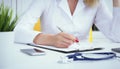 Female medicine doctor hand holding silver pen writing something on clipboard and working laptop closeup. Physician Royalty Free Stock Photo