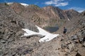 Female millennial hiker stops to use her smart phone while on a nature hike through the mountains, near a large patch of snow and