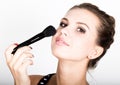 Female model applying makeup on her face. Beautiful young woman applying foundation on her face with a make up brush. Royalty Free Stock Photo