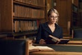 Female model sitting at desk and reading book at library Royalty Free Stock Photo