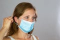 Female model in white shirt attaching surgical face mask on light background