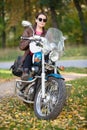 Female motorcycle rider sitting on a classic motorbike, woman with helmet in hands. Portrait in autumn park Royalty Free Stock Photo