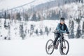 Female mountain biker with bicycle standing outdoors in winter nature.