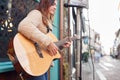 Female Musician Busking Playing Acoustic Guitar Outdoors In Street