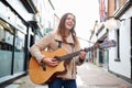 Female Musician Busking Playing Acoustic Guitar Outdoors In Street