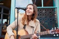 Female Musician Busking Playing Acoustic Guitar And Singing Outdoors In Street