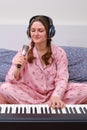 A female musician sings into a microphone and plays the piano on a home bed in the bedroom Royalty Free Stock Photo