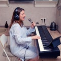 A female musician sings into a microphone and plays the piano in a home kitchen Royalty Free Stock Photo