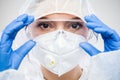 Female NHS doctor,nurse or lab tech virology scientist in PPE,putting on protective eyewear goggles