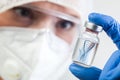 Female NHS microbiologist or lab biotechnician holding glass bottle vial with DNA helix strand floating in liquid