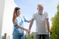 Female nurse or doctor help elderly patient lean to walk with orthopedic walker at outside, patient practice walking in garden Royalty Free Stock Photo