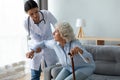 Female nurse help old lady stand up from couch