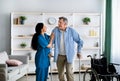 Female nurse helping elderly male to walk with crutches at home. Professional medical care for disabled older patients Royalty Free Stock Photo