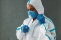 Female nurse in medical respirator zipping white protective suit