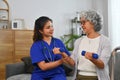 Female nurse or physiotherapist supporting senior woman doing arm exercise for rehabilitation at home.