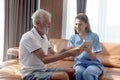 Female nurse takes care of senior patient and teaches him to use digital tablet at living room house, elderly mature grandfather Royalty Free Stock Photo