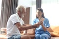 Female nurse takes care of senior patient and teaches him to use digital tablet at living room house, elderly mature grandfather Royalty Free Stock Photo