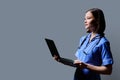 Female nurse using laptop, profile view on gray studio background Royalty Free Stock Photo