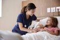 Female Nurse Visiting Girl Lying In Hospital Bed Hugging Teddy Bear