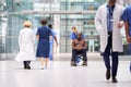 Female Nurse Wearing Scrubs Wheeling Patient In Wheelchair Through Lobby Of Modern Hospital Building Royalty Free Stock Photo