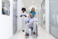 Female Nurse Wearing Scrubs Wheeling Patient In Wheelchair Through Lobby Of Modern Hospital Building. Doctors and nurse in Royalty Free Stock Photo