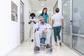 Female Nurse Wearing Scrubs Wheeling Patient In Wheelchair Through Lobby Of Modern Hospital Building. Doctors and nurse in Royalty Free Stock Photo