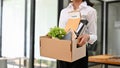 A female office worker holds her cardboard box with stuff and her resignation letter