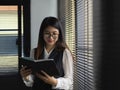 Female office worker reading schedule book while standing next to window Royalty Free Stock Photo