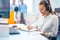 Female operator with headset writing notes while talking to client in customer support center. Royalty Free Stock Photo