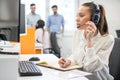 Female operator talking with client via headphones with microphone and writing notes to notebook in call center Royalty Free Stock Photo