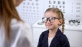 Female optician putting glasses on schoolgirl, little client happy with eyewear