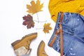 Female orange knitted sweater, blue jeans, boots and autumn leaves on white background top view flat lay. Fashion Lady Clothes Set