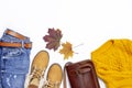 Female orange knitted sweater, blue jeans, leather bag, boots and autumn leaves on white background top view flat lay. Fashion Lad