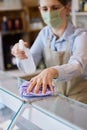 Female Owner Delicatessen Wearing Face Mask Cleaning Counter With Sanitising Spray