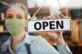 Female Owner Of Small Business Wearing Face Mask Turning Round Open Sign During Health Pandemic