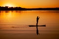 Female paddle boarder moving around with oar in hands on lake with dazzling sunset in background and reflection on