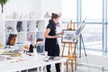 Female painter drawing in art studio using easel. Portrait of a young woman painting with aquarelle paints on white