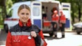 Female paramedic smiling into camera, ambulance crew blurred on background Royalty Free Stock Photo