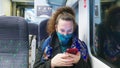 Female passenger wearing face covering mask during covid-19 lockdown using phone inside train in england uk