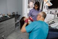 Female patient with open mouth during drilling treatment at the dentist. Professional dental team man and woman doing