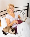 Female pensioner with cat reading book Royalty Free Stock Photo