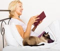 Female pensioner with cat reading book Royalty Free Stock Photo