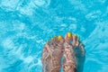 Female with perfect yellow pedicure over a pool. Vacation pericure. Female bare feet in a blue swimming pool water Royalty Free Stock Photo