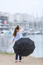 Female person with black umbrella walks along bay in overcast day Royalty Free Stock Photo