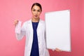 Female person doctor in a white medical coat holding blank board with copy space for text and protective mask isolated Royalty Free Stock Photo